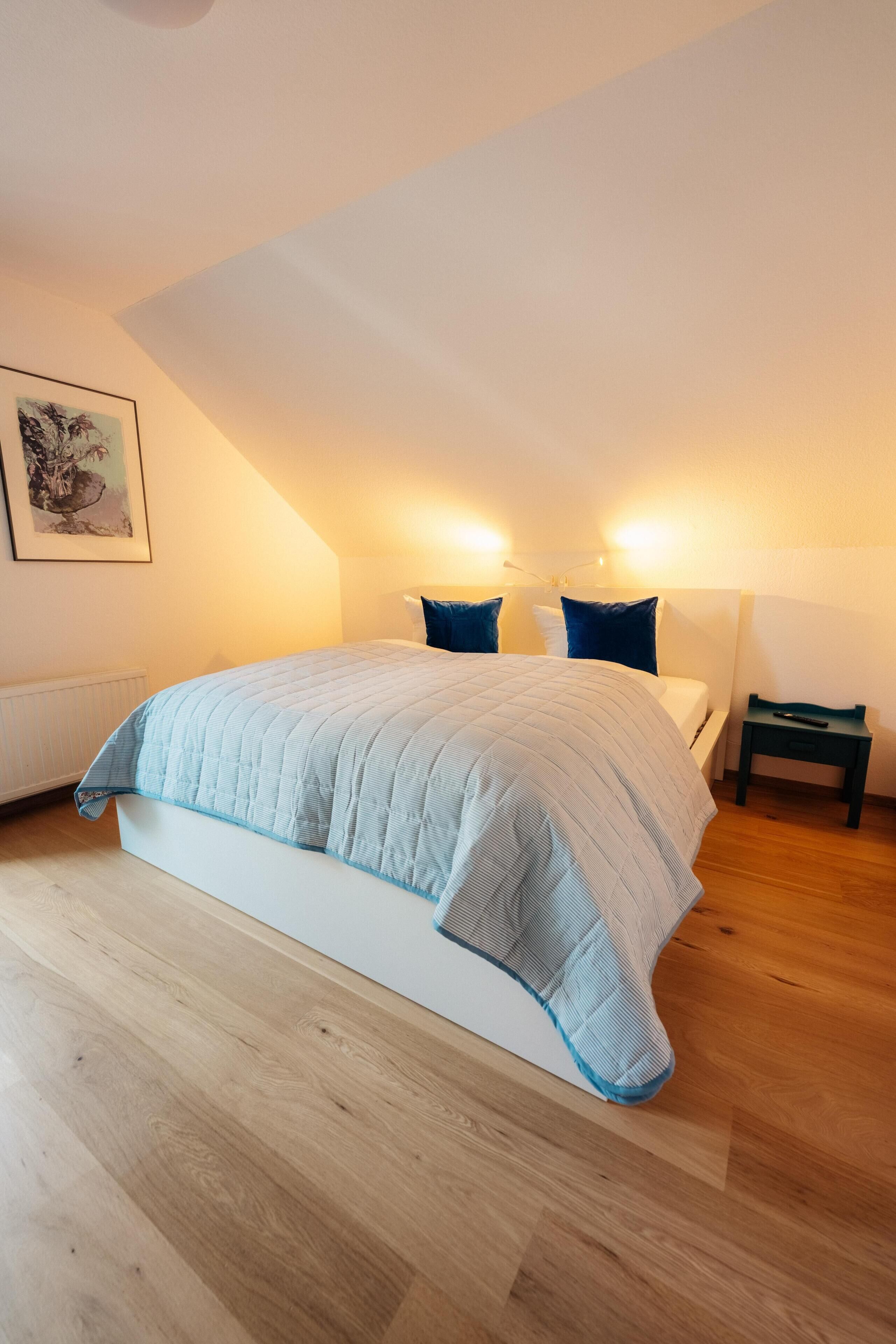 Ein Schlafzimmer mit einem Bett, einem Nachttisch, einer Lampe und einem Bild an der Wand.