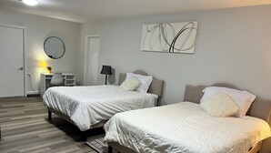 Hotellihuone, jossa on kaksi sänkyä, työpöytä, tuoli, lamppu ja seinätaideteos.