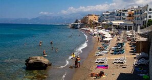 Una playa con tumbonas y sombrillas, una costa rocosa y edificios al fondo.