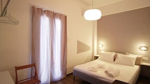 A hotel room with a bed, a chair, a curtain, and a wall-mounted light fixture. - Chersonissos Central Apartment (Hersonissos)