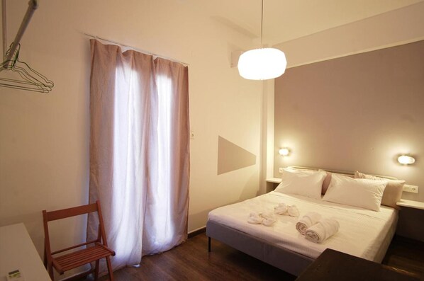 Una habitación de hotel con cama, una silla, una cortina y un aplique de pared.