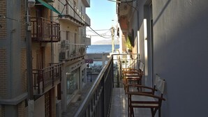 A narrow balcony with wooden chairs, overlooking a street with shops and a view of the sea. - Chersonissos Central Apartment (Hersonissos)
