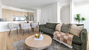 A modern living room with a green sofa, a round coffee table, and a dining area with a kitchen in the background. - Stafford St Apartments by Urban Rest (Adelaide)