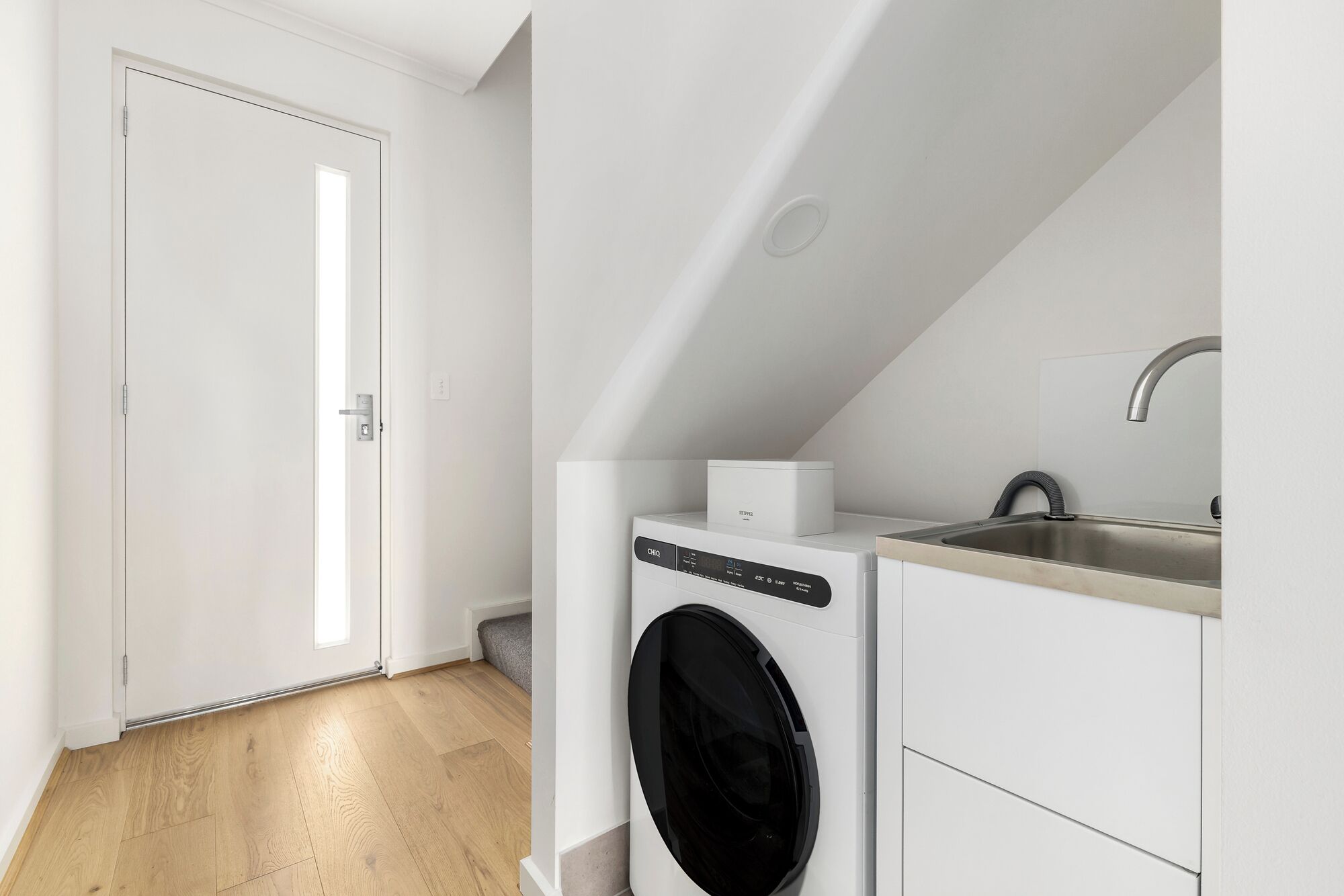Un cuarto de lavandería con lavadora y secadora de carga frontal, un lavabo y una puerta que da a otra habitación.