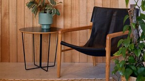 A room with a wooden panel wall, a round table with a potted plant, a black leather chair, and a woven rug. - Secluded Bellbrae sanctuary (Bellbrae)