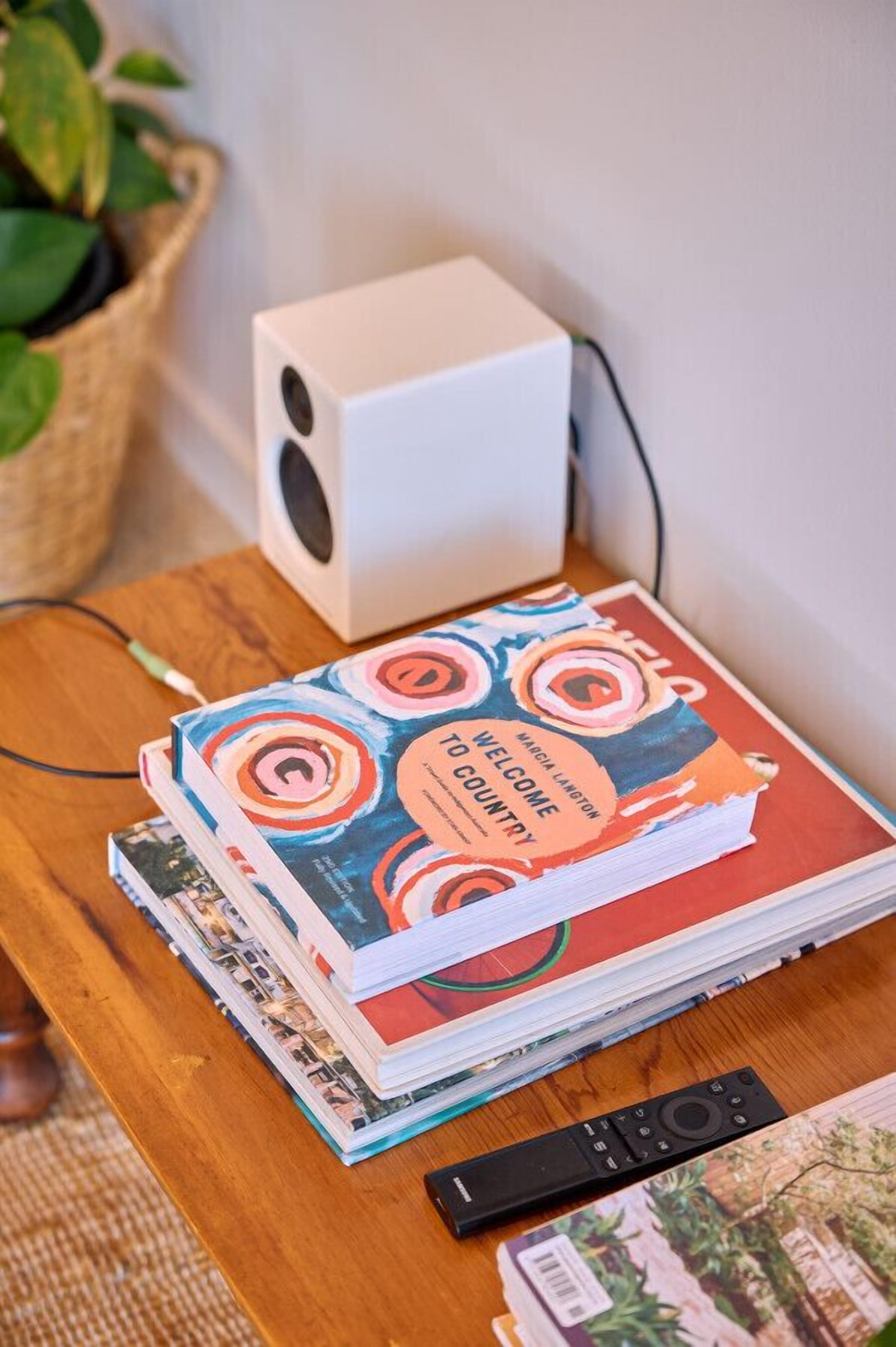 A stack of travel magazines on a wooden table, a remote control, and a white speaker.