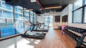 Une salle de sport moderne équipée de tapis de course, d’haltères et de grandes fenêtres donnant sur un paysage urbain.