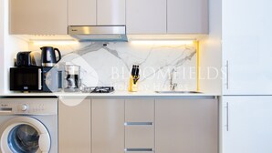 A compact kitchen with a washing machine, microwave, coffee maker, and a gas stove. - Bloomfields STU Riviera Skies In Meydan (Dubai)