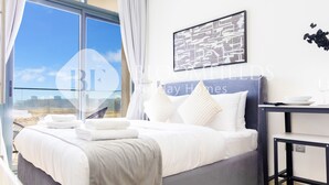 A hotel room with a large window, a bed with white linens, a framed artwork on the wall, and a small table with a bowl and a glass. - Bloomfields STU Riviera Skies In Meydan (Dubai)