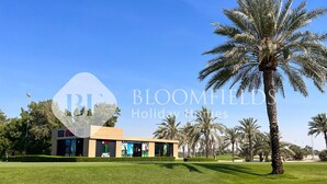A modern building with a flat roof, surrounded by well-maintained grass and palm trees. - Bloomfields STU Riviera Skies In Meydan (Dubai)