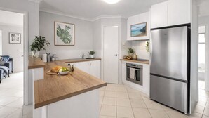 Ett modernt kök med vita skåp, en bänkskiva i trä, ett kylskåp i rostfritt stål och en liten köksö med frukt och en skål.