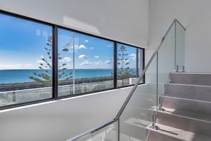 A modern staircase with glass railings leading to a balcony with large windows overlooking a coastal view. - Coastal Bliss with Marina Views-Neaby Cafes (Mandurah)