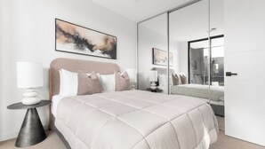 A modern bedroom with a large bed, a bedside table, a mirror, and abstract art on the wall. - Foundry Lane Apartments by Urban Rest (Bowden)