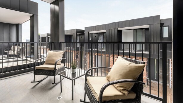 A balcony with wicker chairs and cushions, a potted plant, and a view of the building's exterior. - Foundry Lane Apartments by Urban Rest (Bowden)