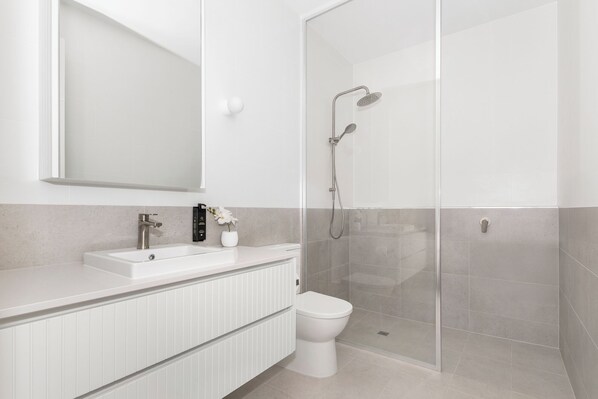 A modern bathroom with a white vanity, a toilet, and a glass-enclosed shower area. - Foundry Lane Apartments by Urban Rest (Bowden)