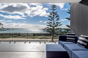 A modern outdoor seating area with a glass balustrade, a blue sofa, and a view of a coastal landscape. - Coastal Bliss: Pet-Friendly, Nearby Cafes with Marina Views (Mandurah)