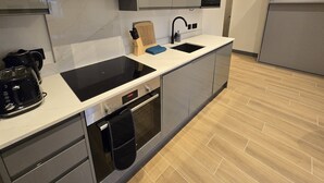 A modern kitchen with grey cabinets, a black countertop, a built-in oven, and a stainless steel sink. - Finchley Perfect 1-Bed - Work & Leisure (London)