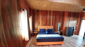 Ein Schlafzimmer mit einer holzverkleideten Wand, einem großen Bett mit blauer Bettwäsche, einem Nachttisch und einem Kühlschrank.