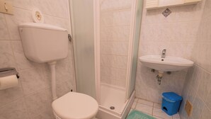 Une salle de bain équipée de toilettes, d’une douche, d’un lavabo et d’une poubelle bleue.