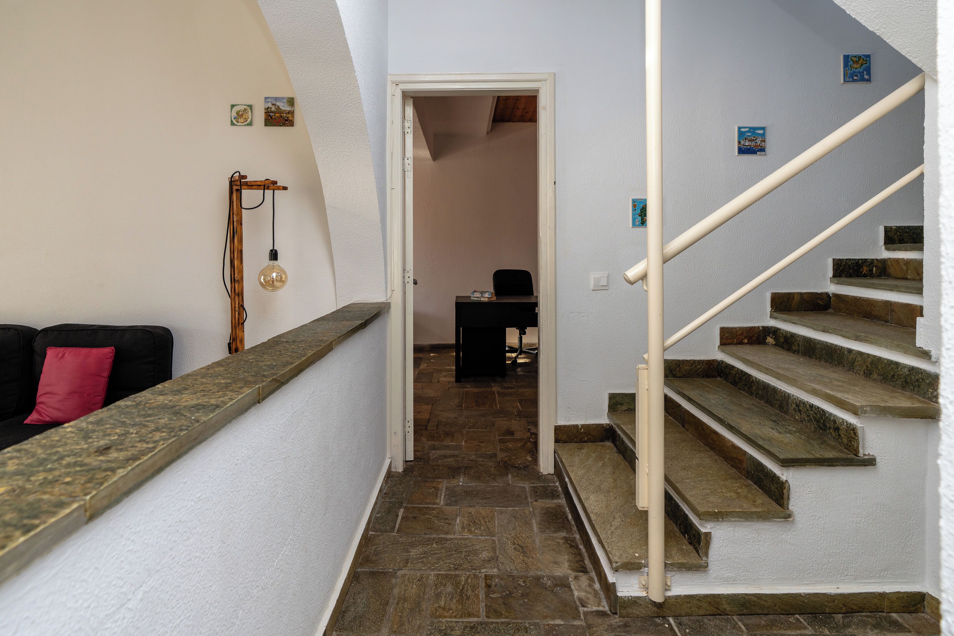 A staircase with stone steps and a white handrail, leading to a room with a desk and chair.