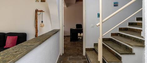 A staircase with stone steps and a white handrail, leading to a room with a desk and chair.