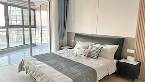 Une chambre moderne avec un grand lit, une table de chevet, une commode et une porte-fenêtre coulissante donnant sur un balcon.