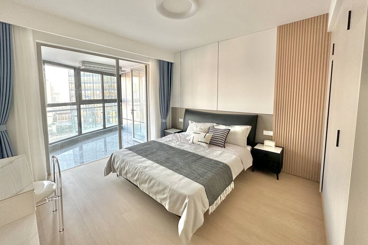 Quarto moderno com uma cama grande, uma mesa de cabeceira, um guarda-roupa e uma porta de vidro deslizante que dá para uma varanda.