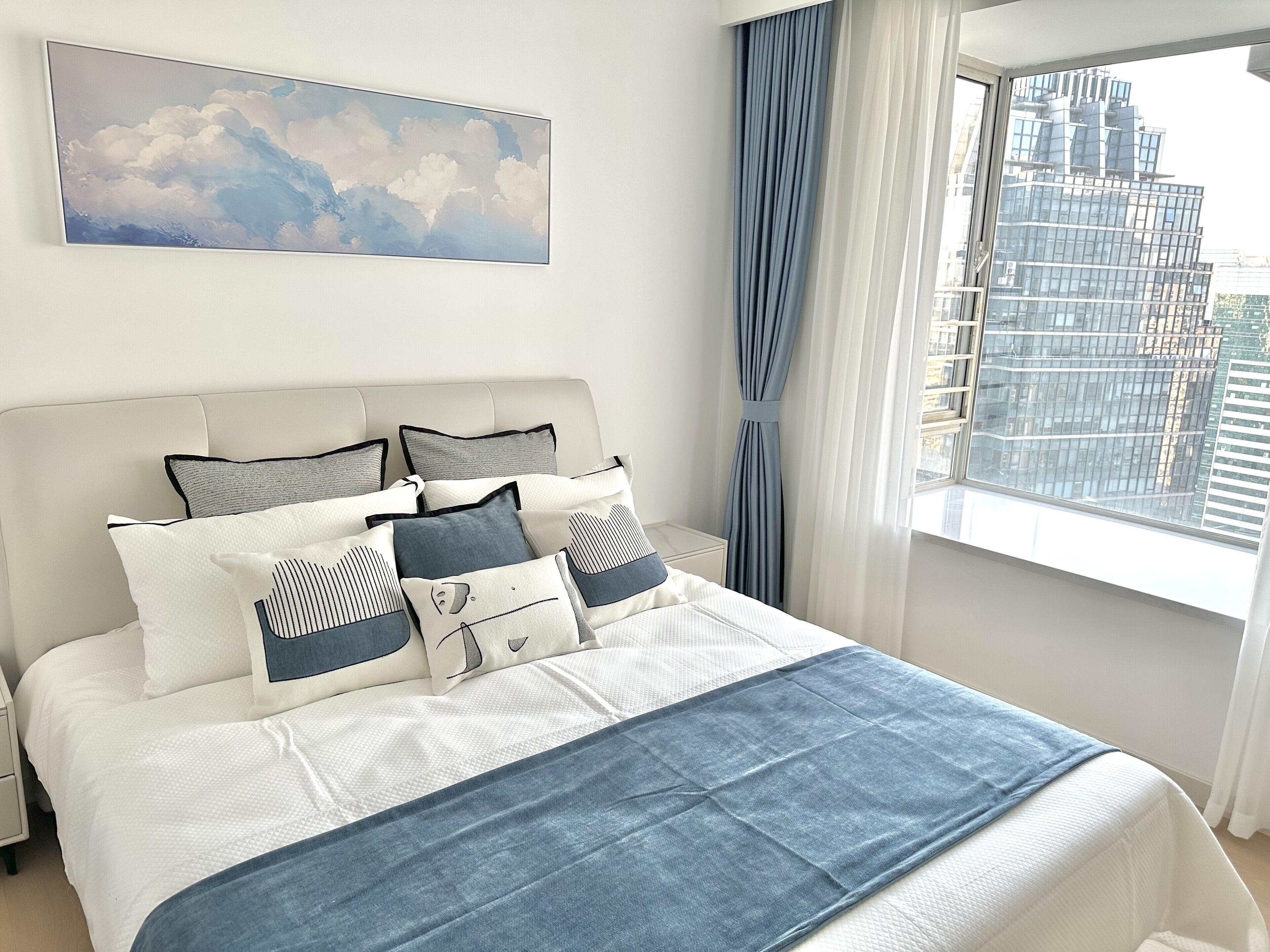 Una cama bien tendida con un cabecero blanco, una colcha azul y varios almohadones.