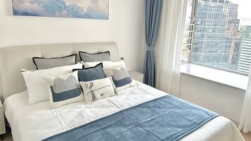 Una cama bien tendida con un cabecero blanco, una colcha azul y varios almohadones.