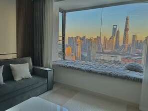 A modern living room with a large window overlooking a city skyline. - ZHome-Shanghai Shining River Apartment (Shanghai)