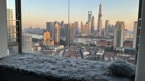 Une vue depuis une fenêtre d’un immeuble de grande hauteur, donnant sur un paysage urbain avec des gratte-ciel modernes, une rivière et une tour historique.