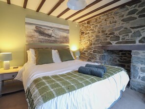 Un dormitorio con pared de piedra, una cama con ropa de cama verde y blanca, un cuadro sobre la cama y una mesita de noche con lámpara.