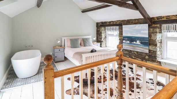 Een slaapkamer met een groot bed, een witte badkuip en een stenen muur.