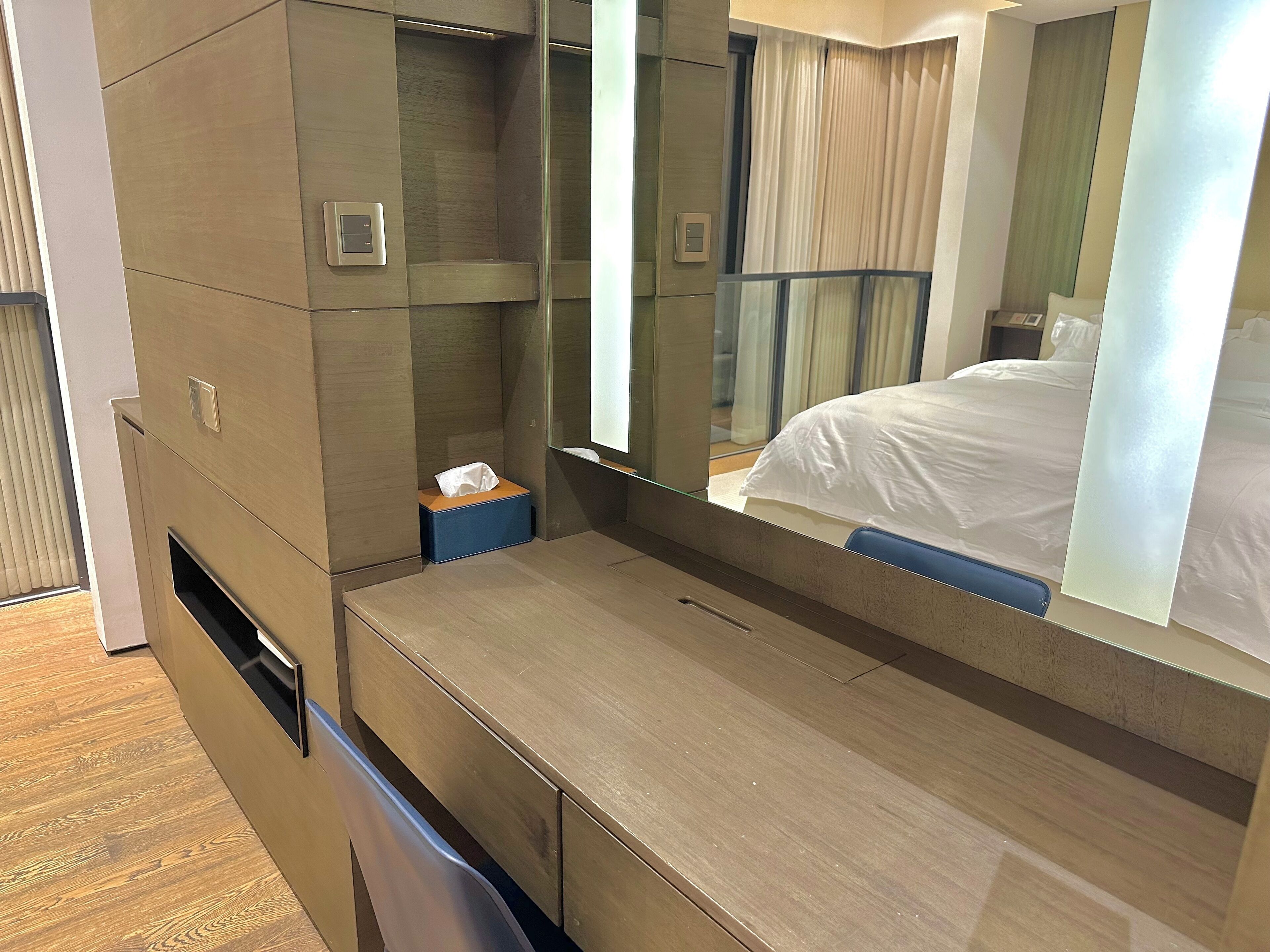 Una habitación de hotel moderna con una cama de madera, un espejo grande y una mesita de noche con una caja de pañuelos.