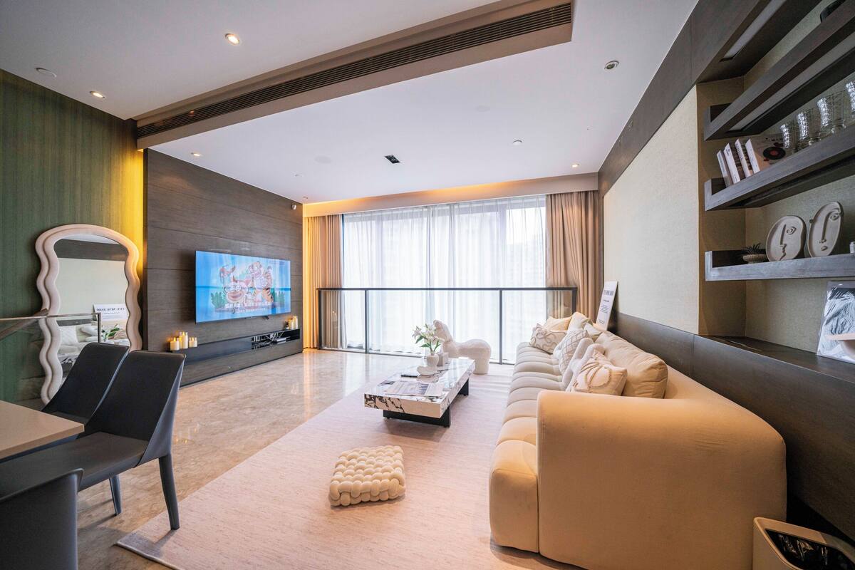 Een moderne woonkamer met een bank, salontafel en een aan de muur bevestigde televisie.