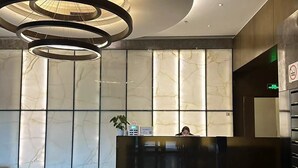 Un vestíbulo moderno con mostrador de recepción de mármol, una lámpara de techo circular y un suelo limpio y reflectante.