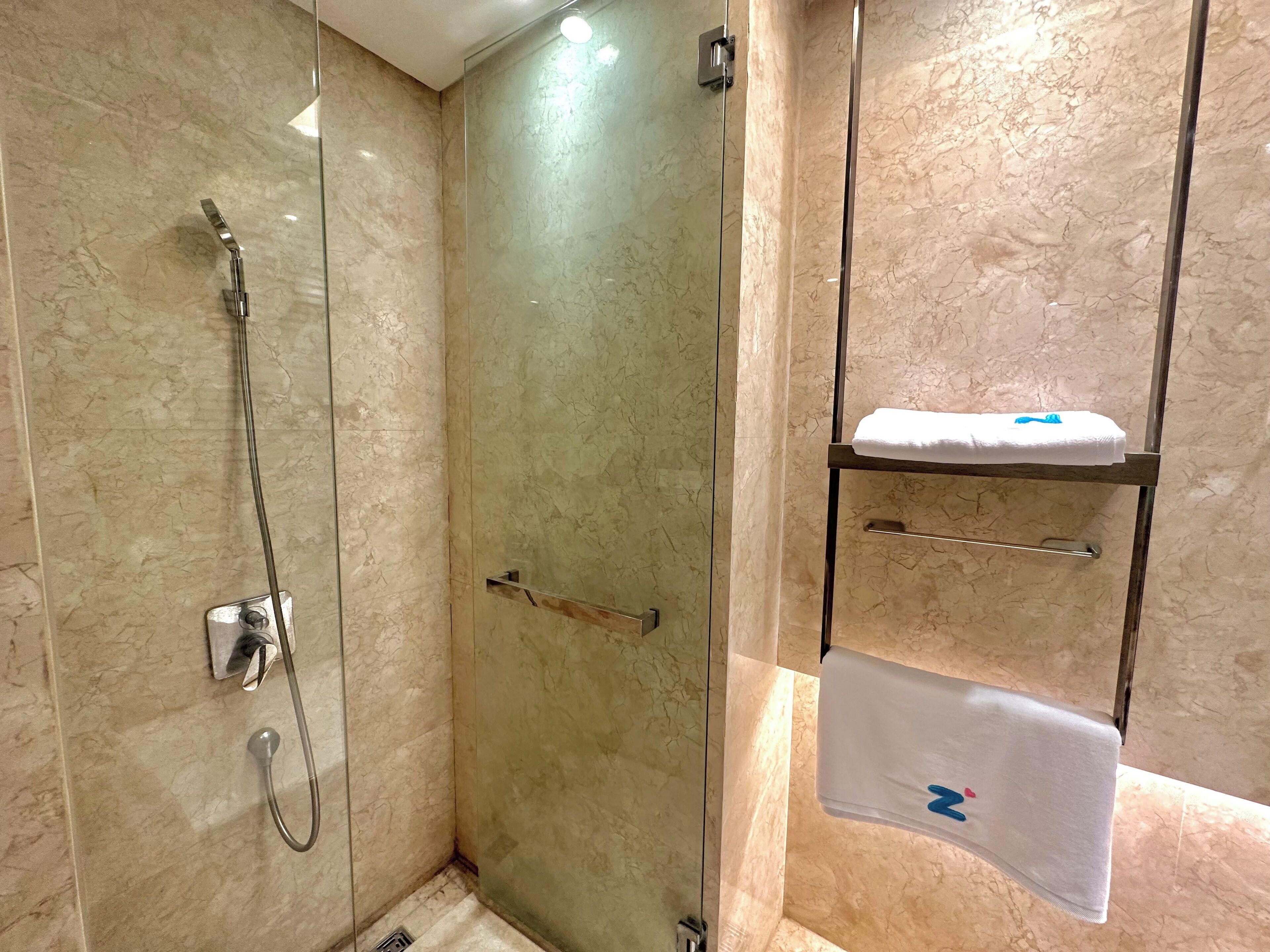A modern bathroom with a glass-enclosed shower, a towel rack with a folded towel, and a marble-tiled wall.
