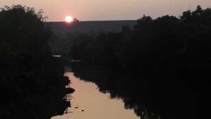 A calm river at sunset with trees on either side and a wooden railing in the foreground. - Alate's guest house (Bhor)