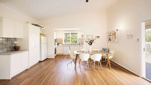 A modern kitchen with white cabinets, a dining area with a white table and chairs, and a ceiling fan.