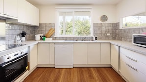 A modern kitchen with white cabinets, a dishwasher, a stove, and a window with a view of trees.