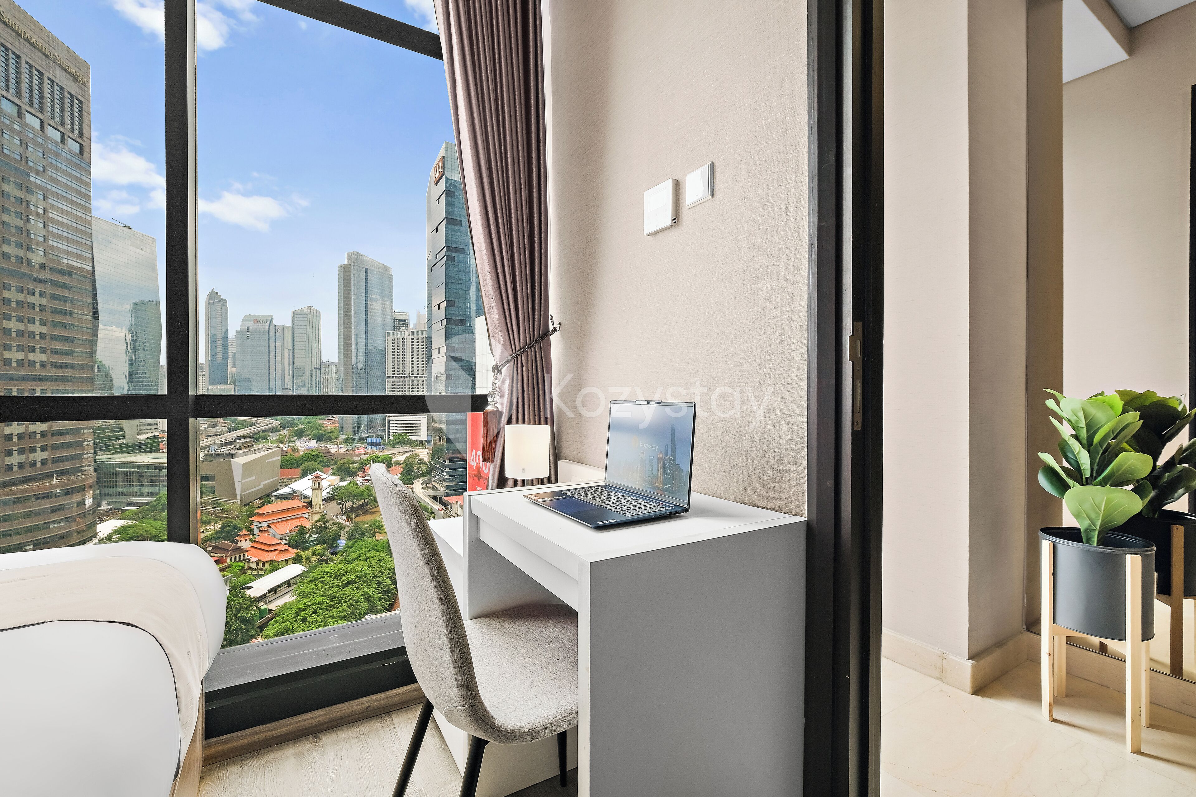 A modern room with a desk, chair, and a laptop. It features a large window with a city view.