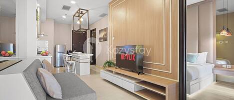 Ein modernes Wohnzimmer mit Flachbildfernseher, einer Couch und einem Essbereich, im Hintergrund befindet sich eine Küche.