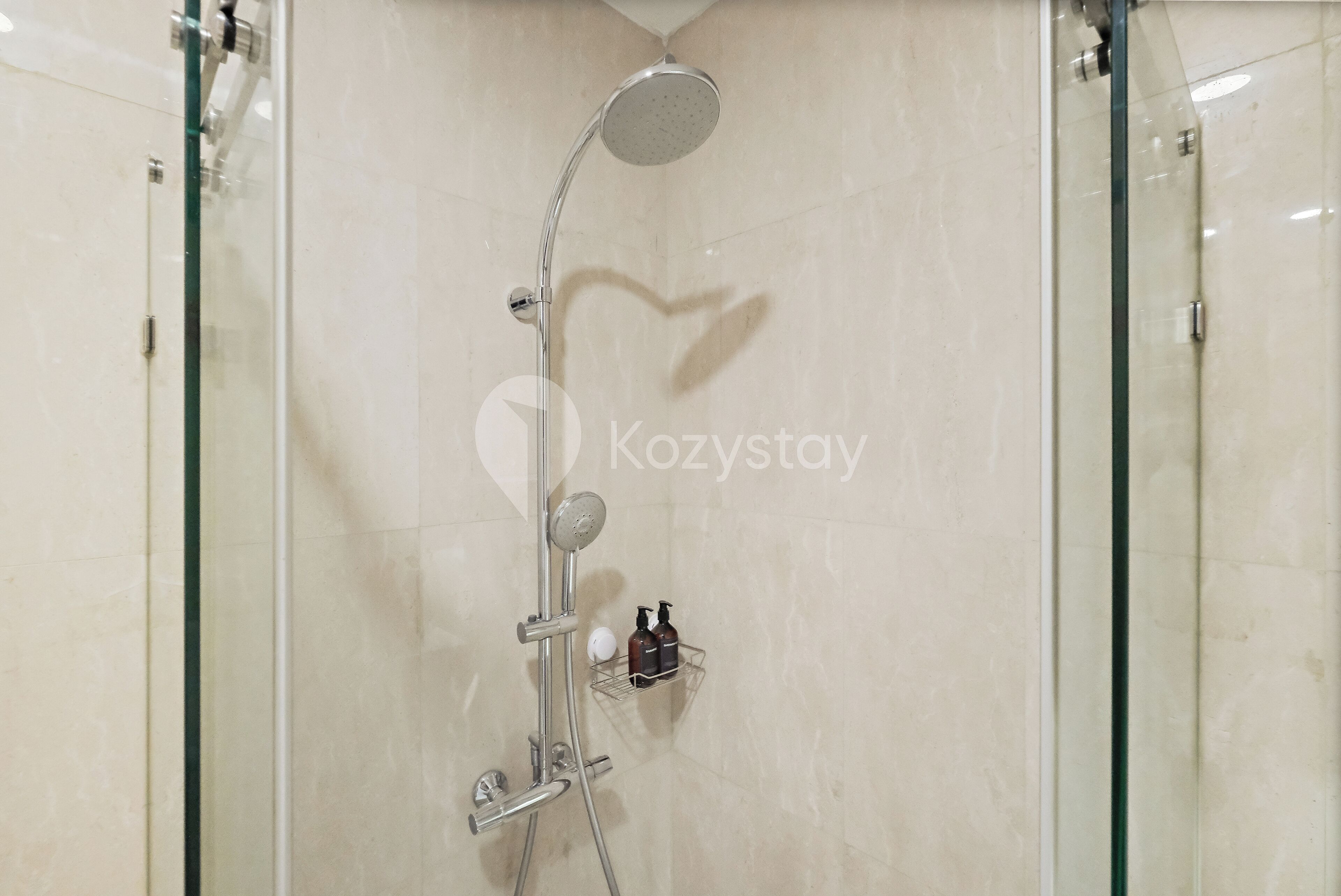 A modern shower with a handheld showerhead, a wall-mounted control panel, and a small shelf with toiletries.