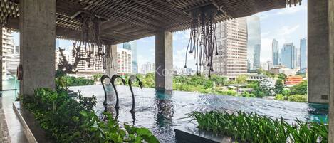 An infinity pool with a city view, surrounded by greenery and a unique wooden ceiling structure.