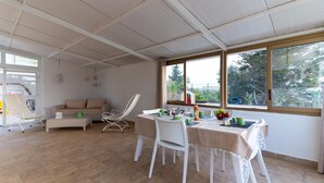 A spacious room with a dining table set for breakfast, a sofa, and a chair. Large windows provide a view of the outdoors. - Panoramic Villa with Infinity Pool – Relax and Comfort in Sicily (Sicilia)