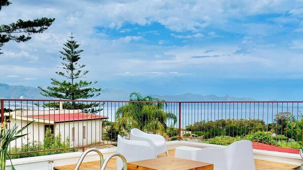 A wooden deck with a pool, white chairs, and a view of the sea and mountains. - Panoramic Villa with Infinity Pool – Relax and Comfort in Sicily (Sicilia)