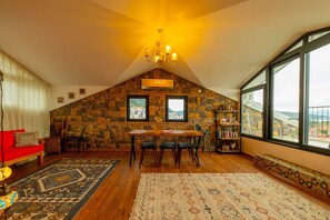A cozy room with a stone wall, a dining table with chairs, a red sofa, and a large window offering a view. - Deniz Loft Fethiye (Fethiye)