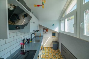 A kitchen with white tiled walls, a patterned floor, a sink, and a window with blinds. - Deniz Loft Fethiye (Fethiye)