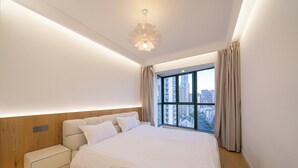 A modern bedroom with a large bed, wooden headboard, bedside tables, and a city view through a large window.