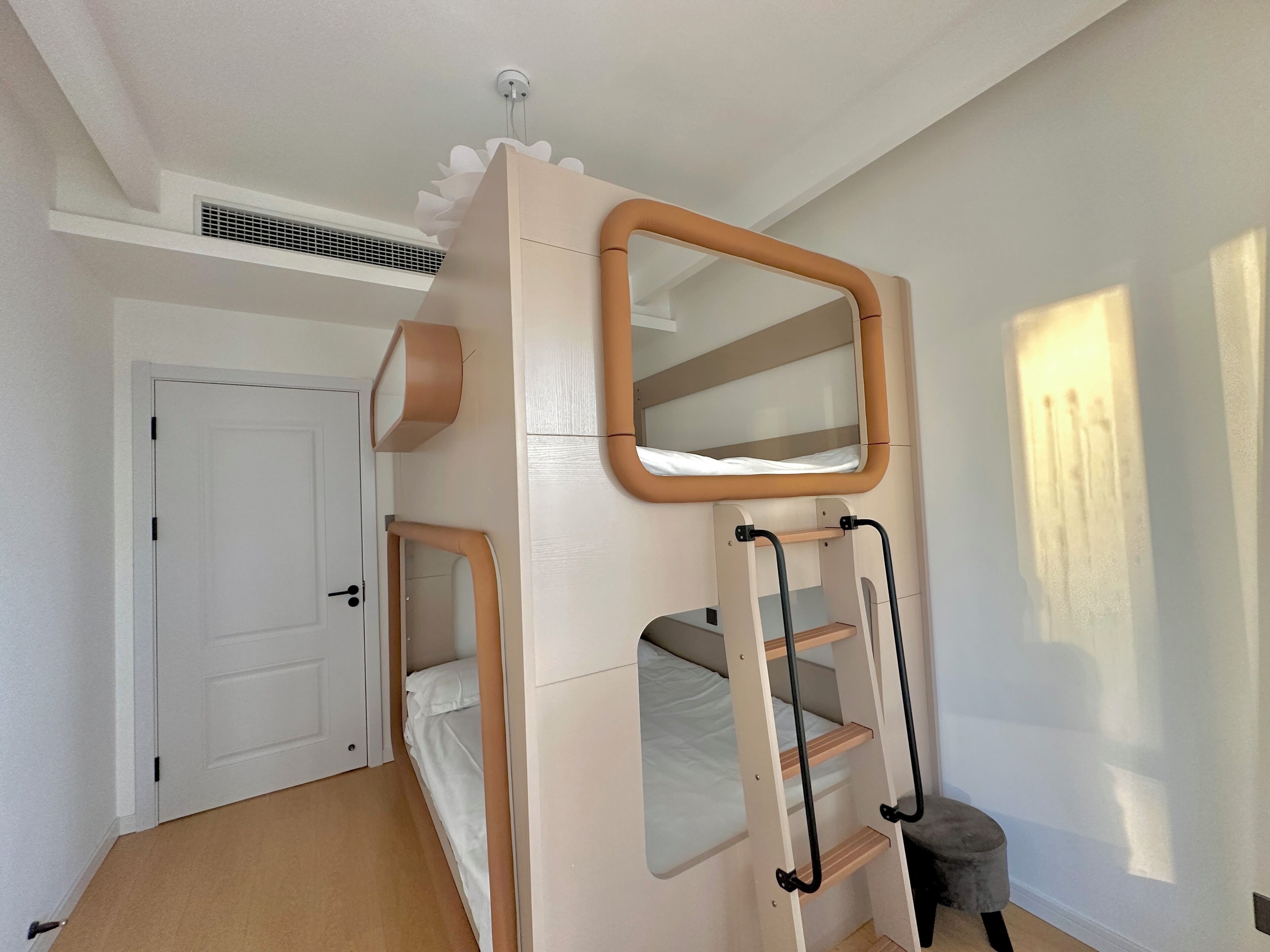 A room with a bunk bed, a ladder, a door, and a window.